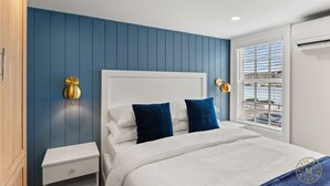 Un dormitorio con una cama blanca, paredes azules y una ventana con vista a la ciudad.