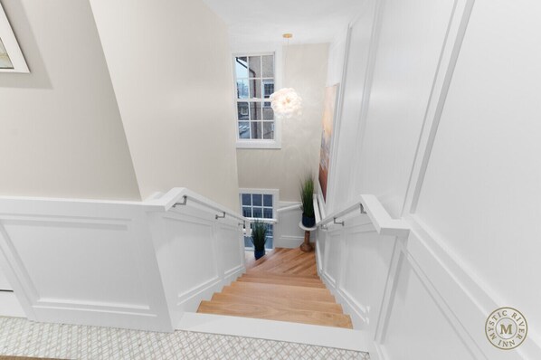 A staircase with white railings and wooden steps leading to a landing with a window and a hanging light fixture.
