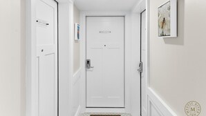 Un pasillo con una puerta blanca, un cuadro en la pared y un felpudo.