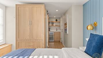 A bedroom with a large bed, a wardrobe, a small kitchenette, and a blue accent wall.