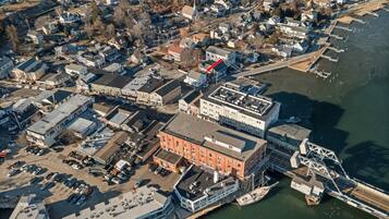 An aerial view of a waterfront area with a prominent red building, a marina with boats, and a bridge connecting to the land.