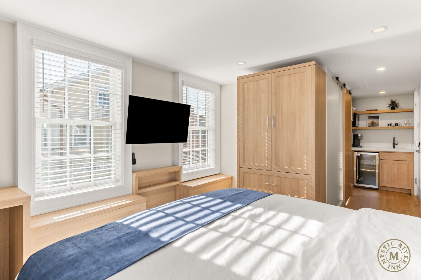 A bedroom with a bed, a TV, a wardrobe, and a kitchenette.