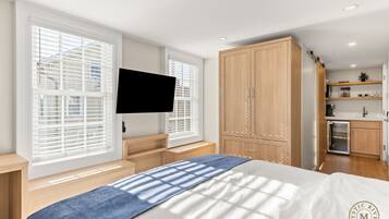 A bedroom with a bed, a TV, a wardrobe, and a kitchenette.