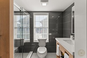 A modern bathroom with a toilet, a shower, and a sink. - The Mystic River Inn (Groton)
