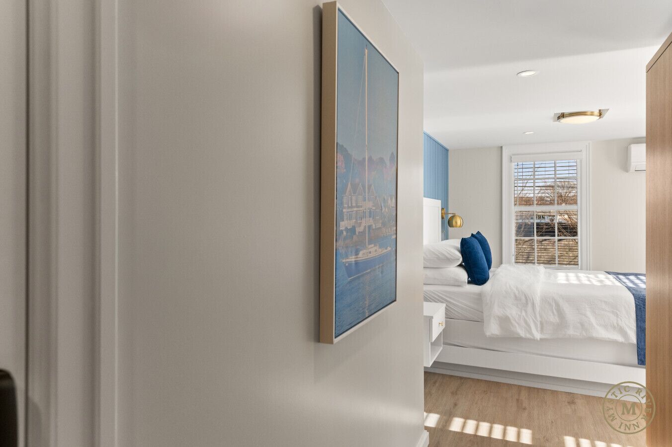 Una habitación de hotel moderna con una cama grande, una mesita de noche, un cuadro enmarcado en la pared y una ventana con persianas.