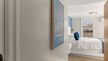 Una habitación de hotel moderna con una cama grande, una mesita de noche, un cuadro enmarcado en la pared y una ventana con persianas.