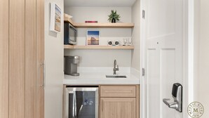 A compact kitchen with a built-in microwave, coffee maker, and dishwasher. There is a wooden cabinet with a glass door, a sink with a modern faucet, and a small shelf with decorative items. - The Mystic River Inn (Groton)