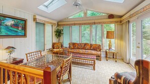 Una veranda luminosa con una grande porta vetrata, un tavolo da pranzo in legno, un divano e una ventola a soffitto.