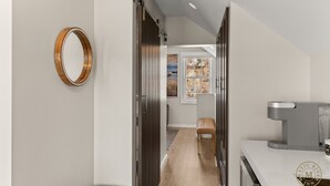 Un pasillo con un espejo de marco de madera, una puerta corredera, vista de una habitación con ventana y un pequeño rincón de descanso.