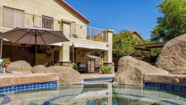 A swimming pool with clear blue water, surrounded by large rocks and a tiled deck. - Group-Ready Glendale Oasis w/ Pool Grotto + Slide (Glendale)