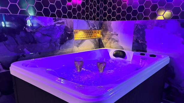 Un jacuzzi con dos copas de champán, rodeado por una pared de azulejos hexagonales con diseño de panal.