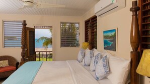 Una camera da letto con un letto, una sedia di legno, un ventilatore a soffitto e vista sulla spiaggia.