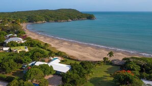 Una vista aerea di una proprietà costiera con spiaggia, una piccola isola e una zona boschiva.