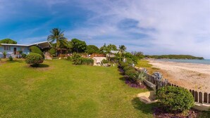 Una proprietà fronte spiaggia con una casa, un prato curato e una spiaggia sabbiosa.