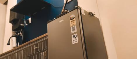 A compact refrigerator with a warranty sticker, placed in a room with a blue accent wall and a radiator.