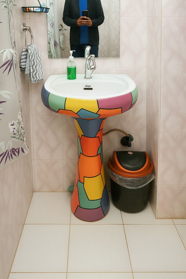 A bathroom with a uniquely designed sink, a hand soap dispenser, and a trash bin.
