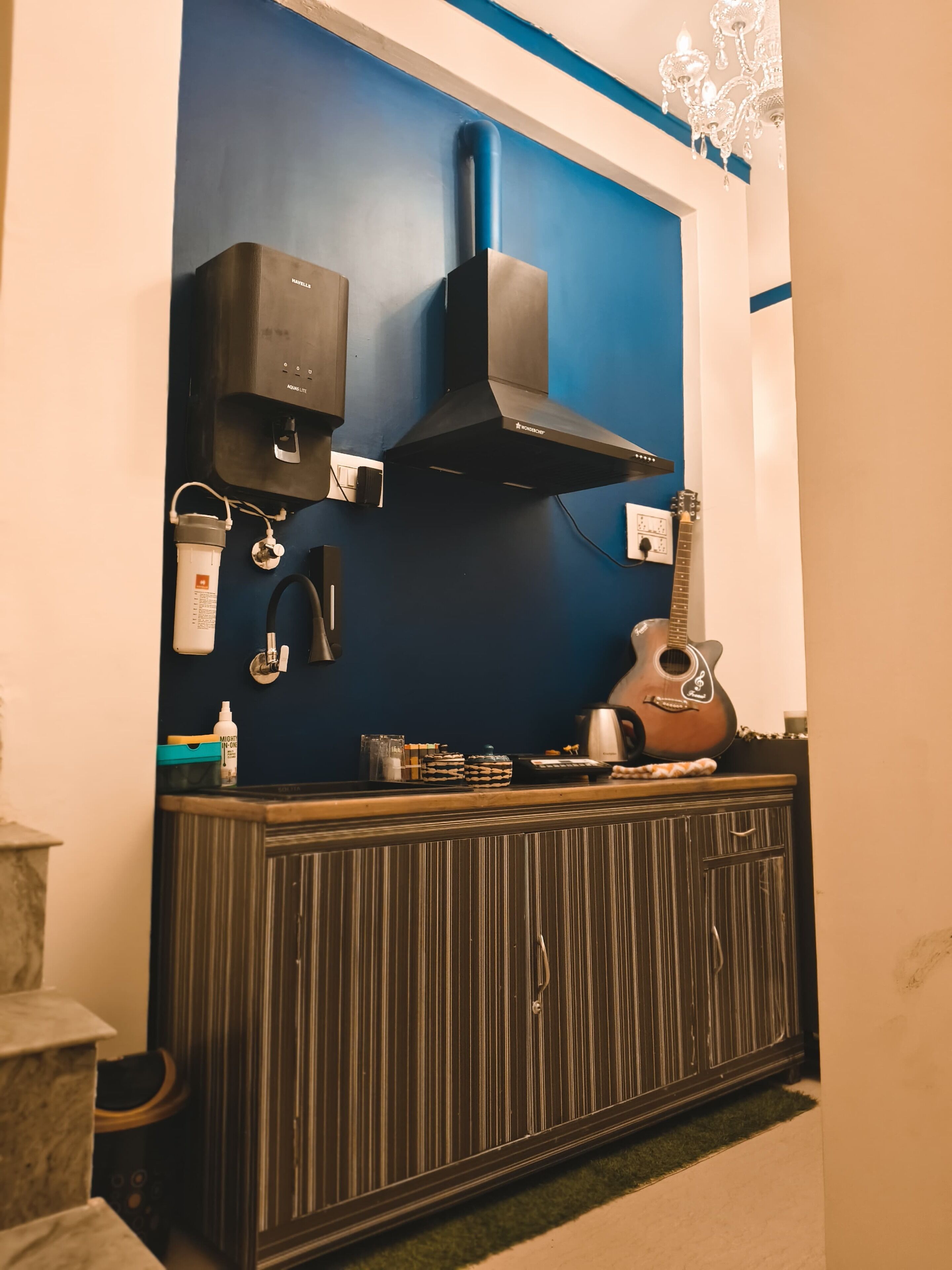 Una cocina con pared azul, extractor negro, una guitarra y diversos objetos de cocina sobre la encimera.
