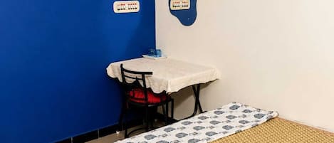 A room with a bed, a table, a chair, a clock, and a wall-mounted air conditioner.