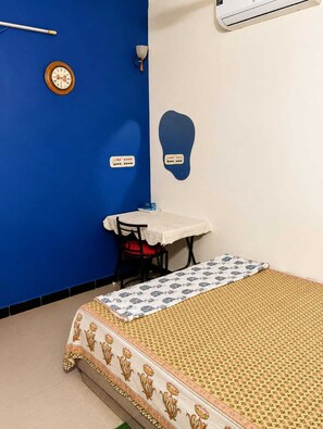 A room with a bed, a table, a chair, a clock, and a wall-mounted air conditioner.