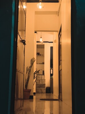 A hallway with a potted plant, a light fixture, and a door at the end. - Veena Vihar (Full House) (Jodhpur)