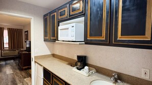 Una cocina con armarios de madera oscura, un microondas blanco, una cafetera y un lavamanos.