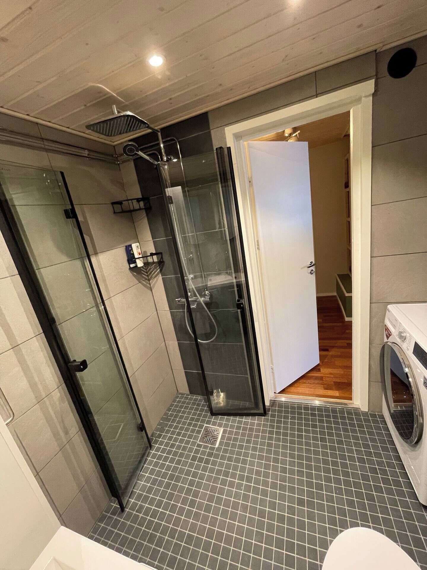 A modern bathroom with a glass shower enclosure, a built-in washing machine, and a tiled floor.