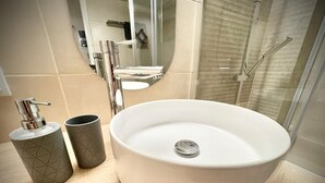 Een badkamer met een rond wit wastafel, een spiegel en een douchehoek.