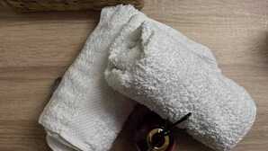 Een houten tafel met een mand waarin toiletpapier, een fles handzeep en een grijze handdoek liggen.