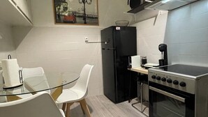 Een kleine keuken met een eettafel, stoelen, een koelkast, een fornuis en een magnetron.