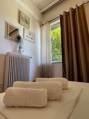 Une chambre d’hôtel avec un lit, deux serviettes, un radiateur, un miroir et une fenêtre avec des rideaux.