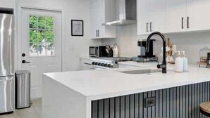 Een moderne keuken met witte kasten, een centraal eiland met krukken, een roestvrijstalen koelkast en hangende lampen.