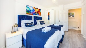A bedroom with two beds, a nightstand, a lamp, and a colorful abstract painting on the wall. - A Nice Apartment in Central London, Great For Sightseeing (London)