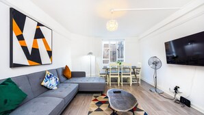 A modern living room with a gray sofa, a geometric wall art, a dining area with a table and chairs, and a flat-screen TV mounted on the wall. - A Nice Apartment in Central London, Great For Sightseeing (London)