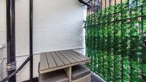 Een hoekje met een tafel en een rieten bankje, een witte bakstenen muur en een wand van groene planten.