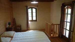 Ein Schlafzimmer mit einem großen Bett, einem kleinen Tisch mit Lampe, einem Fenster mit Vorhängen und einem Holzbalken.