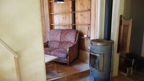 Ein gemütliches Zimmer mit einem gemusterten Sessel, einem kleinen Tisch und einem Kaminofen.
