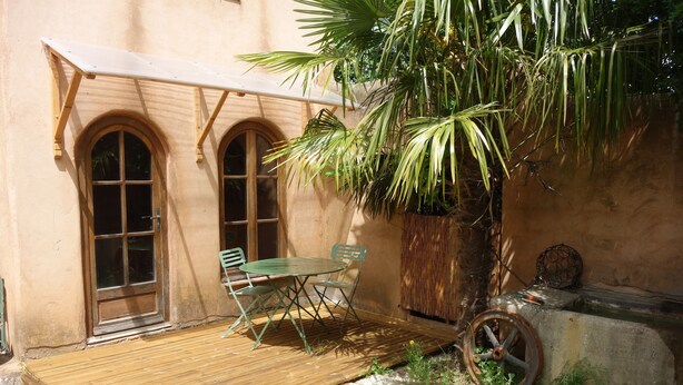 Eine Holzterrasse mit Tisch, Stühlen, einer Palme und einem alten Fahrradrad.