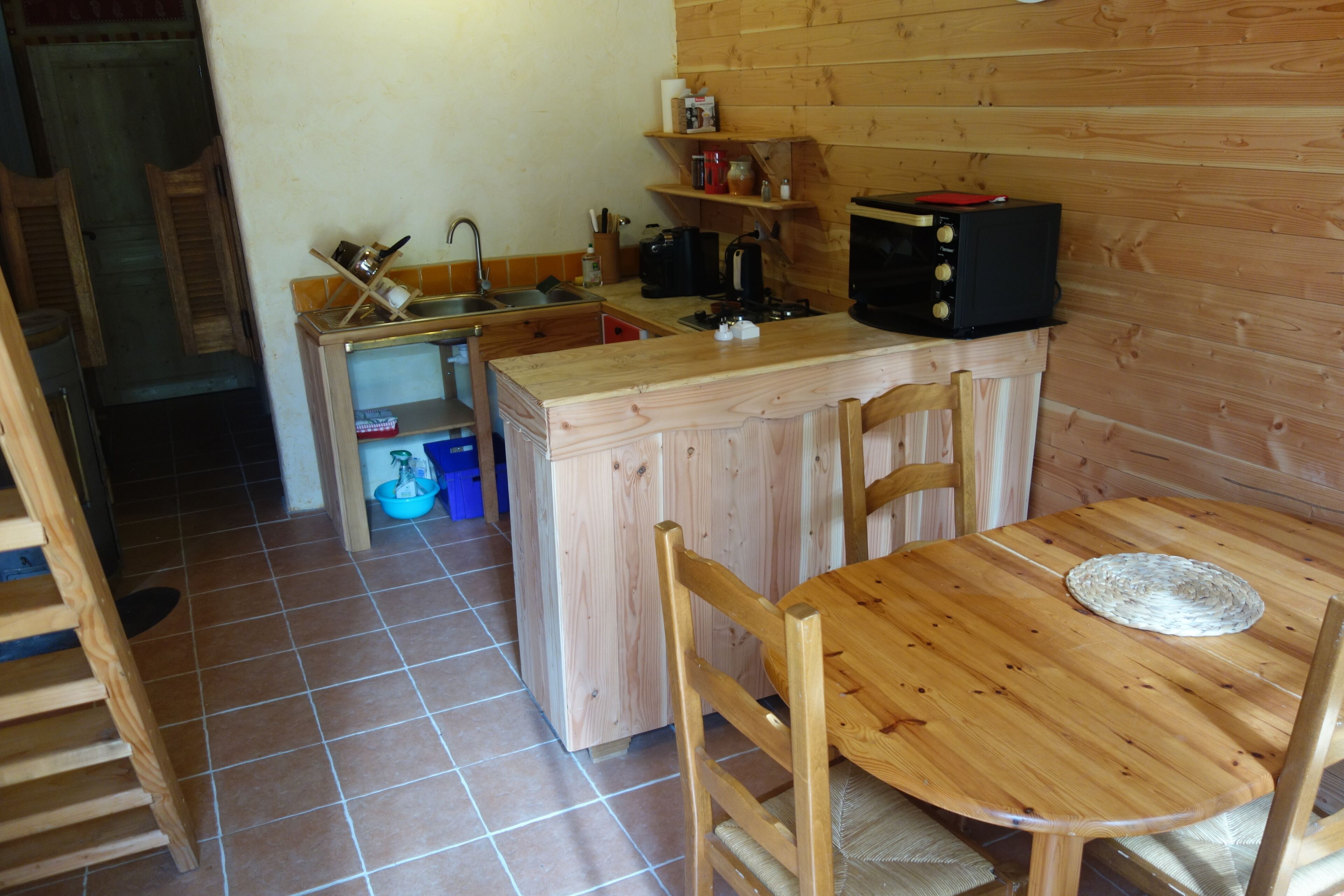 Une cuisine compacte avec des meubles en bois, un évier, une cuisinière et un four à micro-ondes. On y trouve une table à manger avec des chaises et un lavabo bleu.
