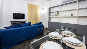 Ein modernes Wohnzimmer mit einem blauen Sofa, einem Flachbildfernseher, einem Kamin und einem Essbereich mit Tisch für zwei Personen.