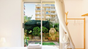 Hotelkamer met een bed, een raam met uitzicht op een balkon, een houten droogrek en een potplant.