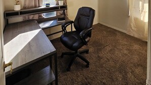 Ein Zimmer mit Schreibtisch, Stuhl und einem Vorhangfenster.