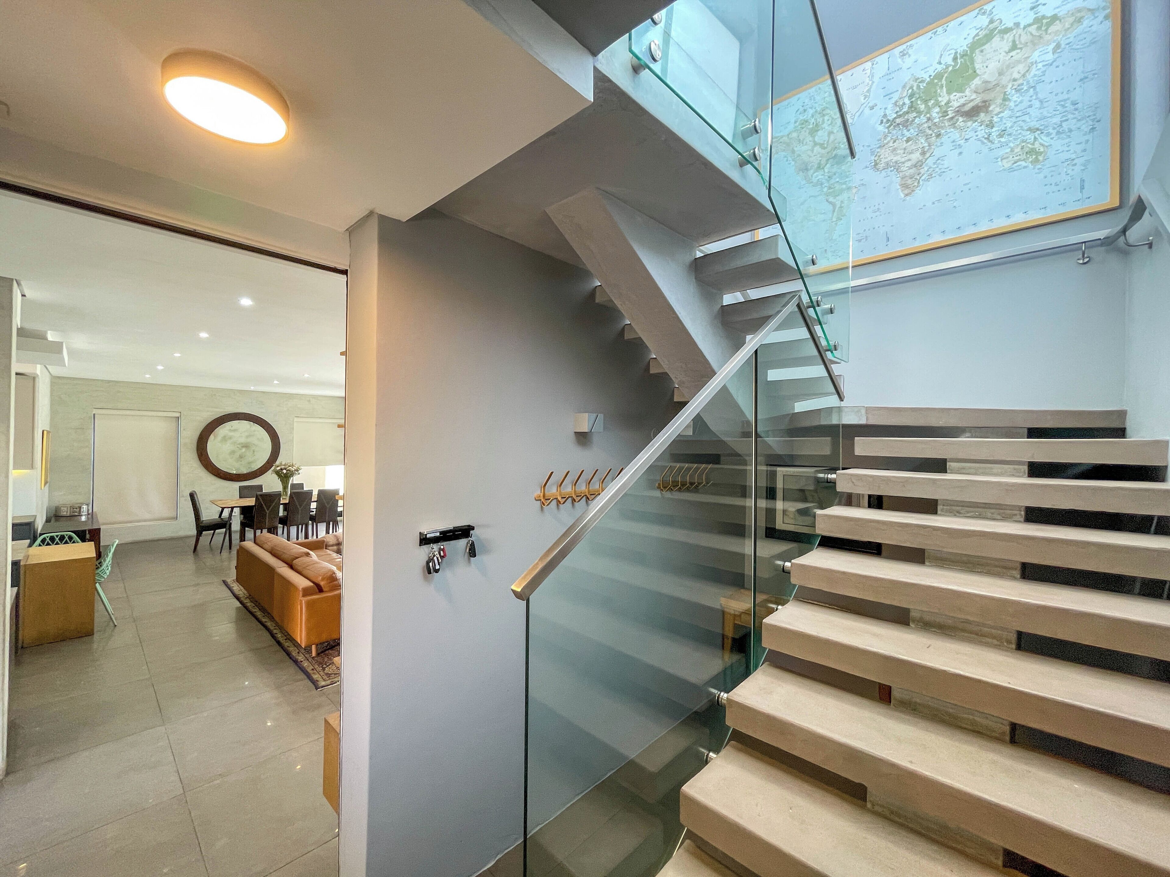 Un intérieur moderne avec un escalier en verre, un coin repas et une carte accrochée au mur.