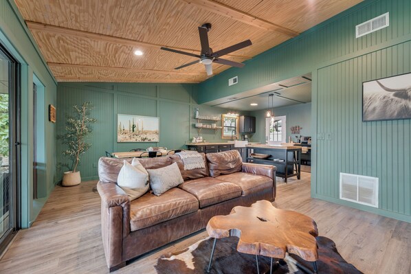 A spacious living area with a brown leather sofa, a wooden coffee table, and a ceiling fan. - NEW listing Lake retreat. Sunset views, Turf, Fire Pit, & Cedar Party Pavilion. (Gun Barrel City)