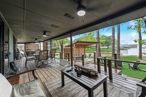 A covered outdoor area with wooden flooring, tables, chairs, and a view of a lake. - NEW listing Lake retreat. Sunset views, Turf, Fire Pit, & Cedar Party Pavilion. (Gun Barrel City)