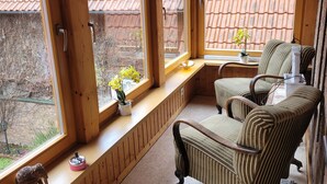 A cozy room with large windows, a wooden bench, a striped chair, and a small table with a plant.
