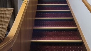 A wooden staircase with a patterned carpet, a framed artwork on the wall, and a potted plant on the left.