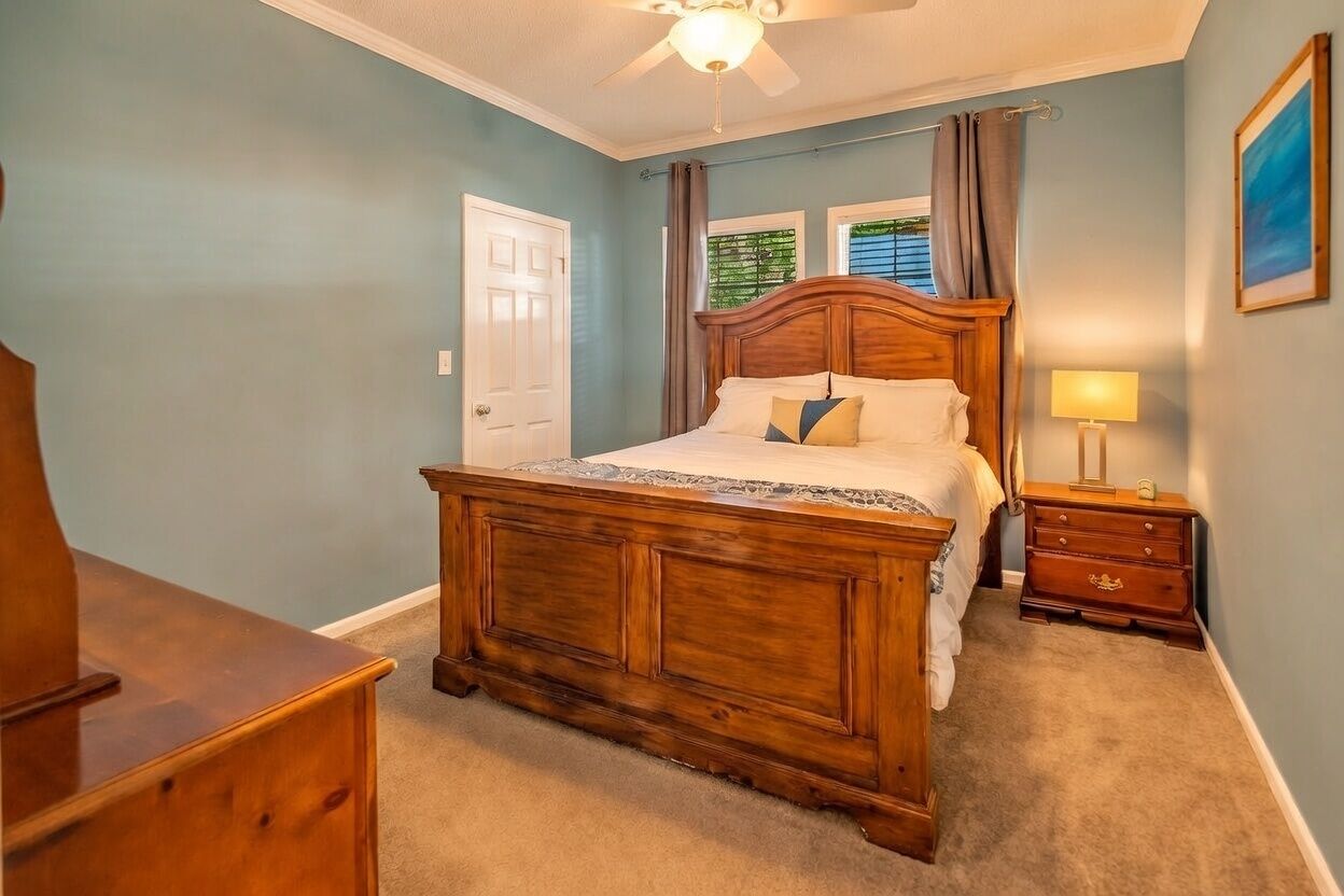 Une chambre à coucher avec un lit en bois, une table de chevet avec une lampe, une porte et une fenêtre avec des rideaux.