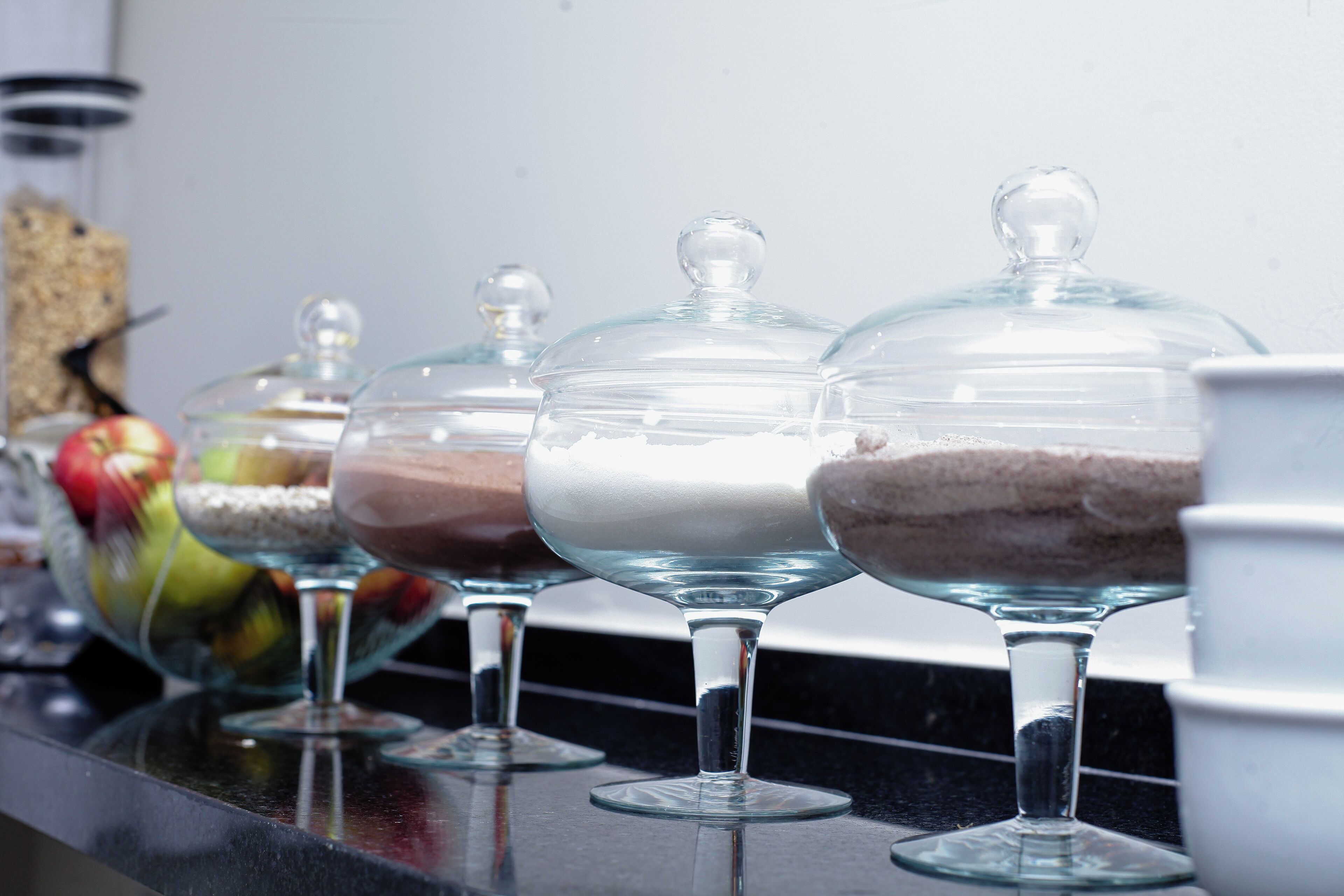 A row of glass dessert bowls with lids on a countertop.