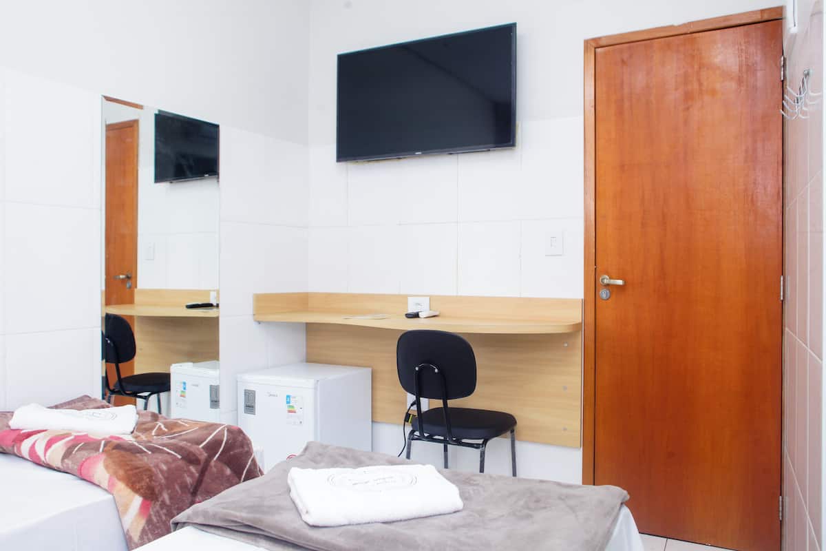 Una camera d'albergo con un letto, una scrivania, una sedia, una televisione e un armadio.