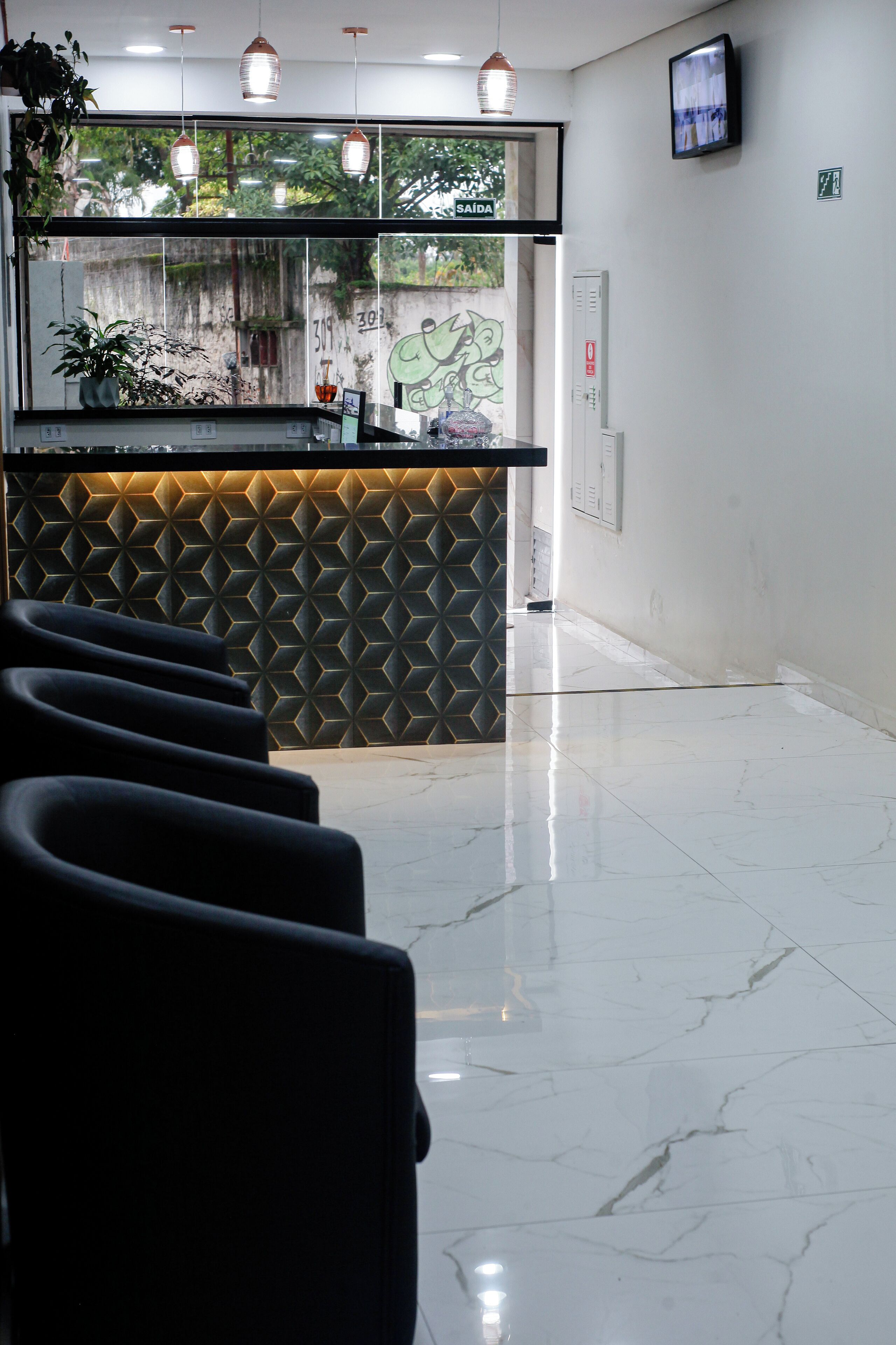A reception area with a modern design, featuring a geometric patterned wall, a reception desk, and a row of black chairs.